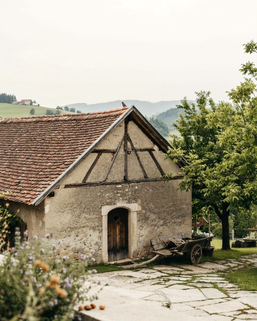 Small Styrian stone cottage with timber gable, heart-cut door and wooden cart