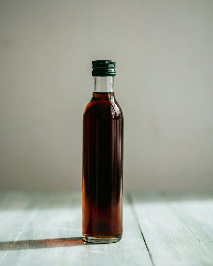 Clear glass bottle of dark Styrian pumpkin seed oil on light wood