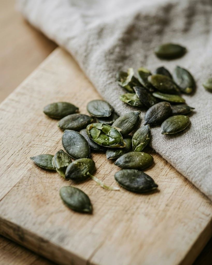 Dark green Styrian pumpkin seeds on light wood with linen