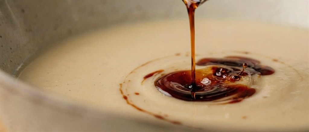Thin stream of dark pumpkin seed oil pouring onto creamy soup